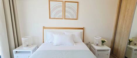 A bedroom with a bed, two nightstands, a mirror, and two framed artworks on the wall.