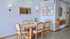 A dining area with a wooden table and chairs, a vase of flowers, and wall-mounted artwork. - Coastal Waves - Relaxing 3BR Apartment with pool & Ocean Views (Praia)