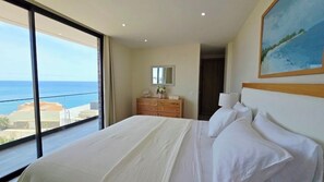 A bedroom with a large bed, a dresser, a mirror, and a painting. - Coastal Waves - Relaxing 3BR Apartment with pool & Ocean Views (Praia)
