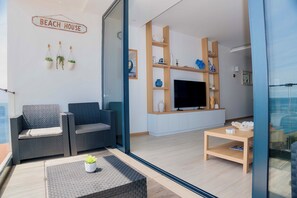 Una sala de estar moderna con un sofá, una mesa de centro y un televisor. Hay plantas en macetas y objetos decorativos en estantes.