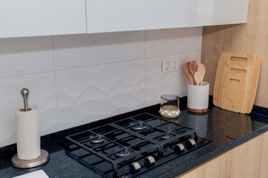 Una cocina con estufa a gas, un rollo de toallas de papel, utensilios de madera y una tabla de cortar.