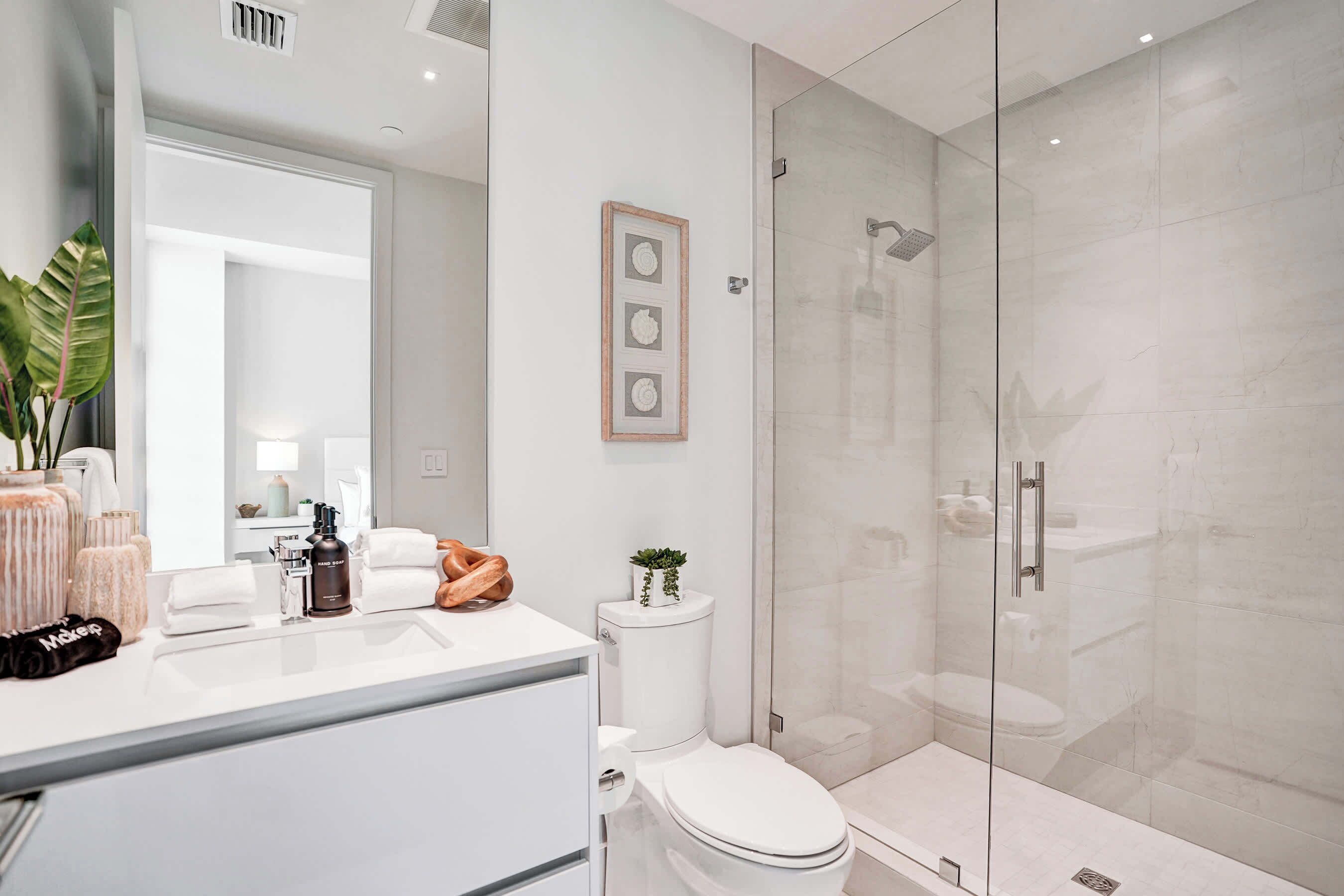 A modern bathroom with a glass shower enclosure, a white toilet, and a vanity with a mirror and toiletries.