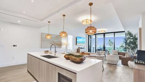 Cozinha moderna com ilha central, iluminação pendente e vista para a sala de estar.