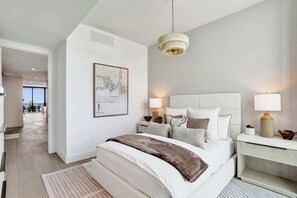 Ein modernes Schlafzimmer mit einem großen Bett, Nachttischlampen, einer Deckenleuchte und Blick ins Freie.