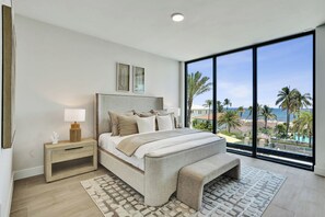 A bedroom with a large bed, a nightstand, a bench, and a view of the ocean. - Oceanview Escape 3BR Near Pompano Beach (Pompano Beach)