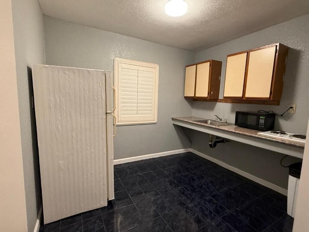 A compact kitchen with a refrigerator, a microwave, and wooden cabinets.
