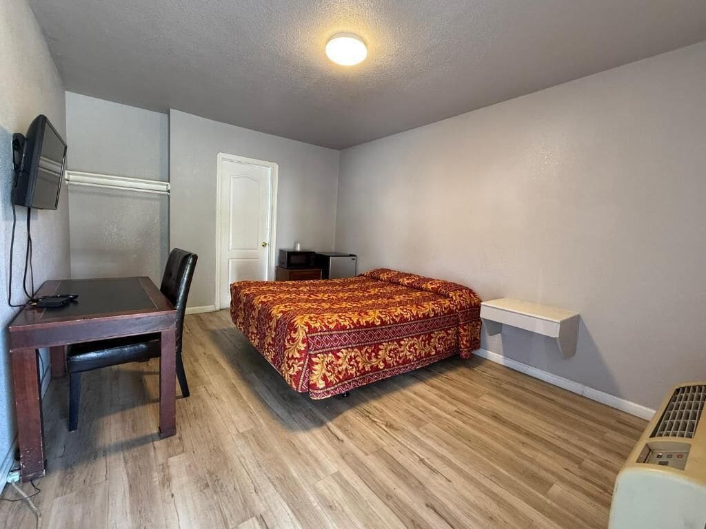 Une chambre à coucher avec un lit, un bureau, une chaise, une porte et une petite étagère.