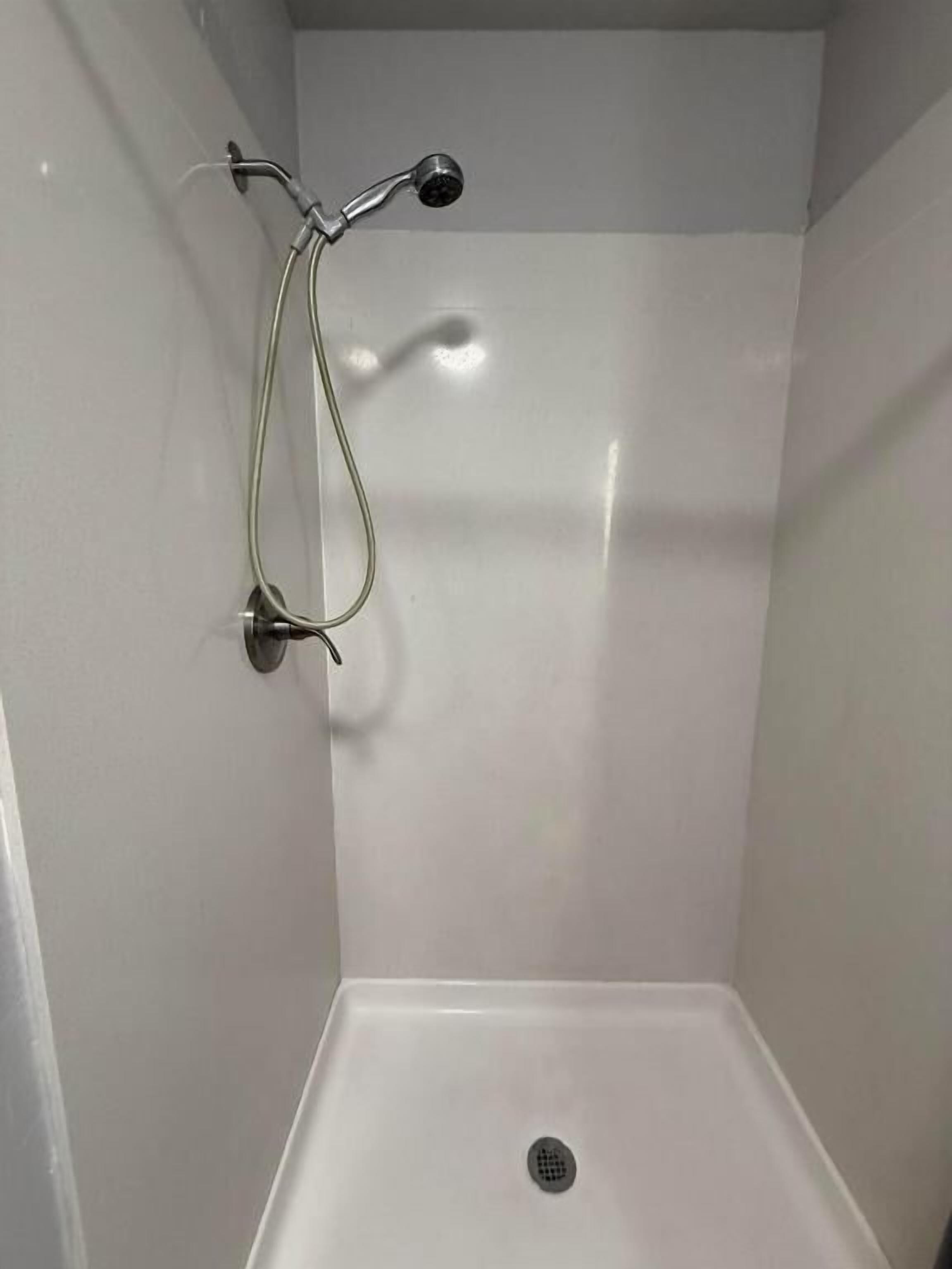 A shower with a handheld showerhead and a wall-mounted faucet.