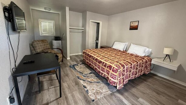 Een slaapkamer met een bed, bureau, stoel, televisie en lamp.