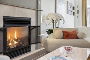 A modern living room with a fireplace, a sofa with cushions, a coffee table, and a potted orchid plant. - Elegant 2BR+Office Leaside Home|Free Parking.Ravine.NearLRT. Sunnybrook Hospital (Toronto)