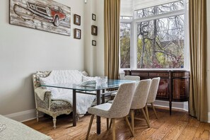 A dining area with a glass table, two upholstered chairs, a vintage sofa, and a view through a bay window. - Elegant 2BR+Office Leaside Home|Free Parking.Ravine.NearLRT. Sunnybrook Hospital (Toronto)