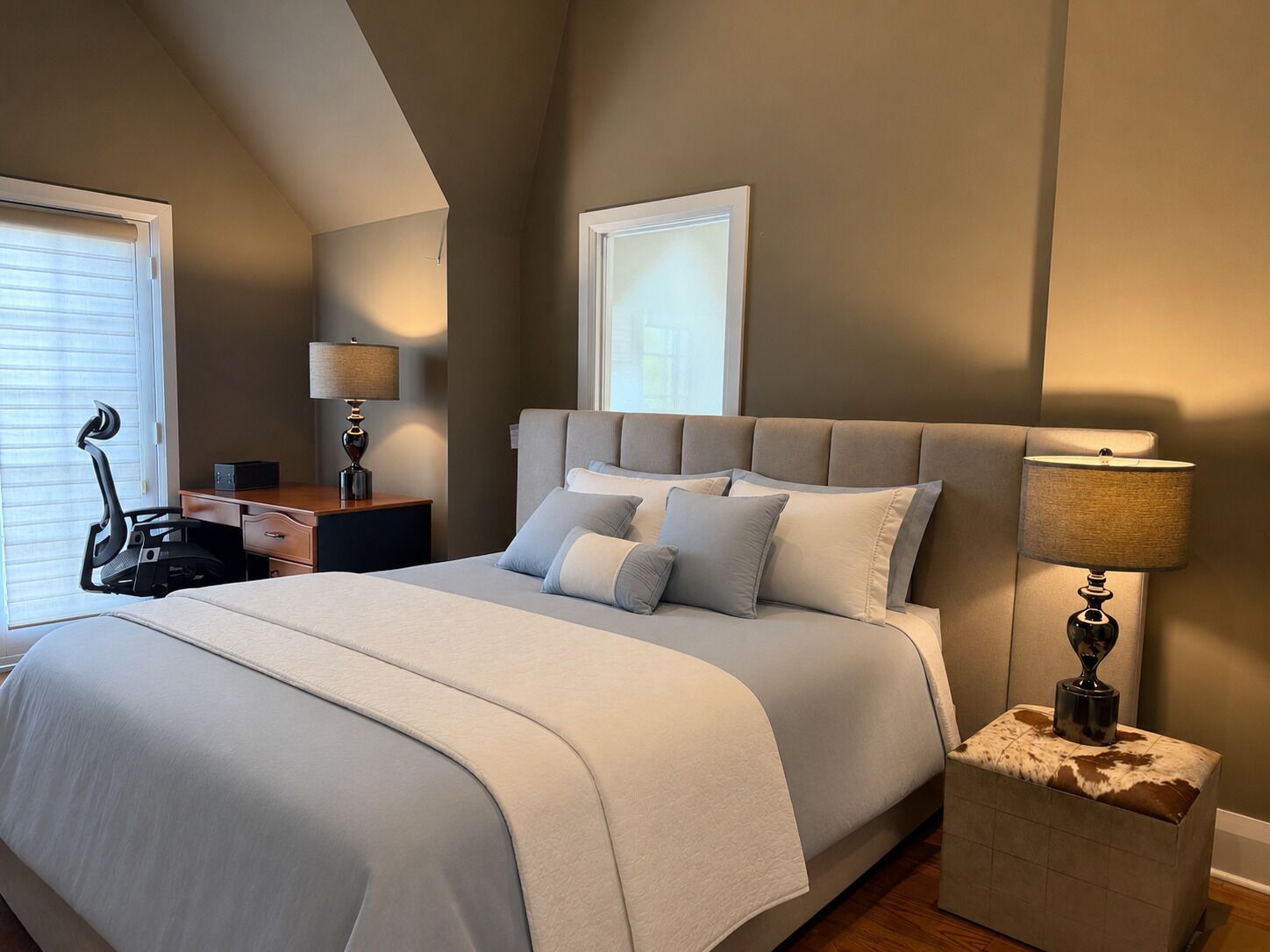 A bedroom with a large bed, a desk, a chair, and a lamp.