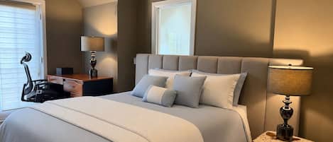 A bedroom with a large bed, a desk, a chair, and a lamp.