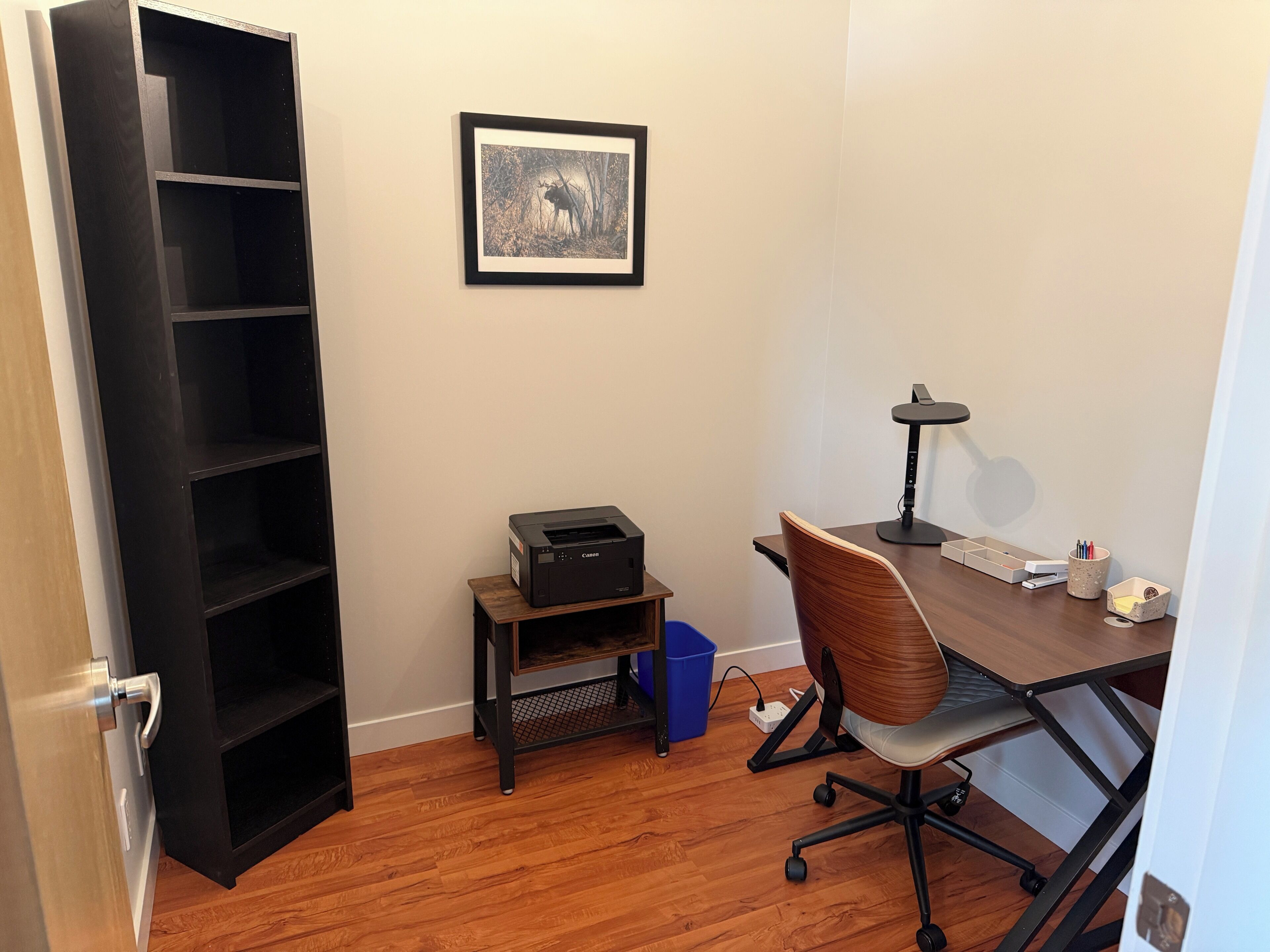 A room with a desk, chair, printer, and a framed picture on the wall.