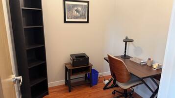 A room with a desk, chair, printer, and a framed picture on the wall.