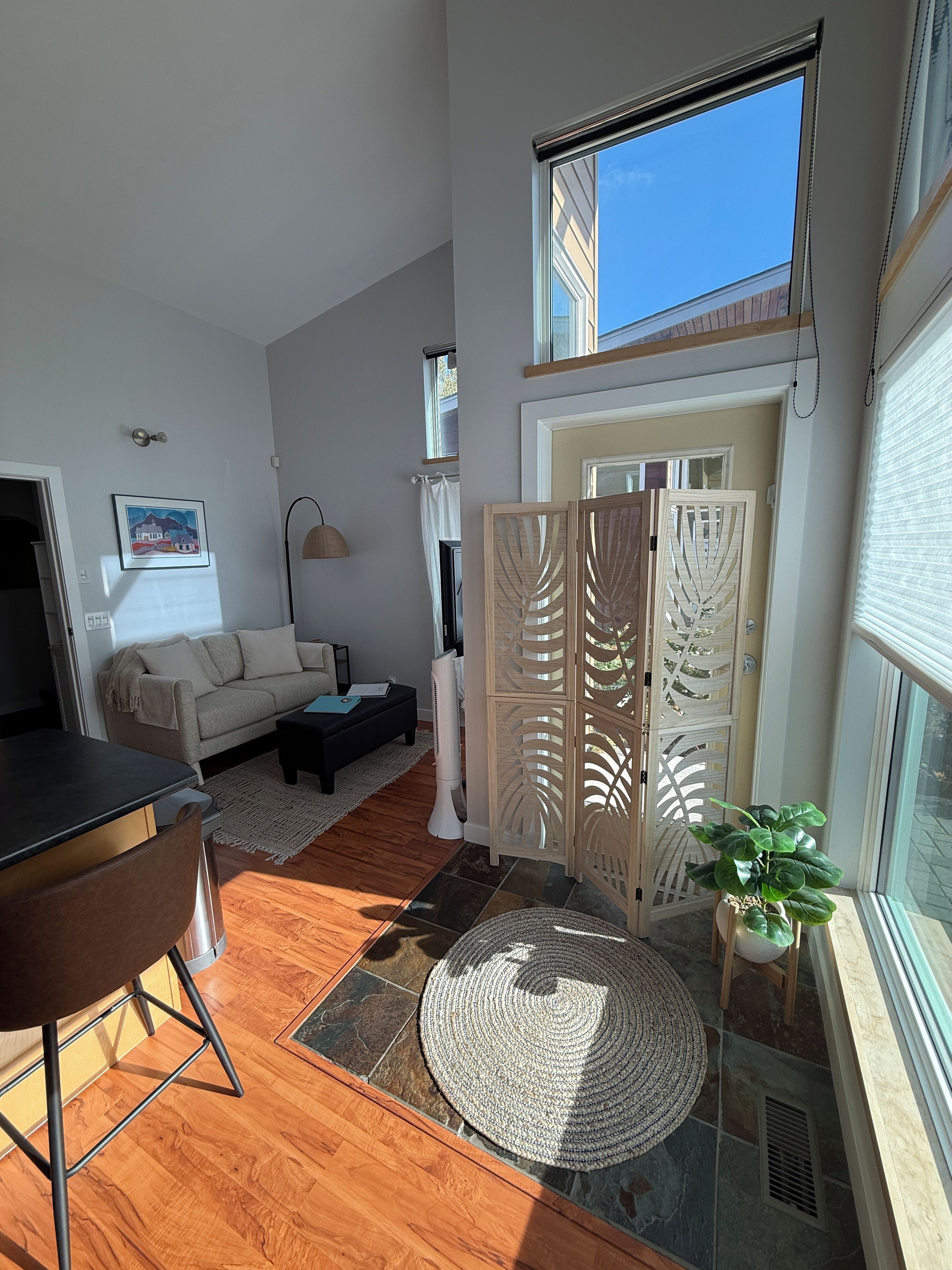 A spacious living area with a high ceiling, a dining table, a sofa, a coffee table, and a potted plant.
