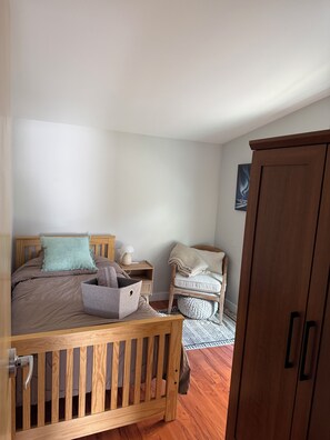 A bedroom with a wooden bed, a nightstand, a chair, a wardrobe, and a wall-mounted picture.