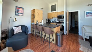 Un espacio habitable compacto con kitchenette, un área de comedor con taburetes de bar, un sofá y un cesto de basura.