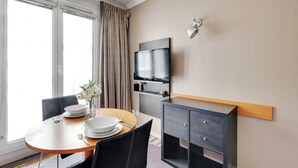 A hotel room with a dining table set for two, a television mounted on the wall, and a small cabinet with drawers. - Modern Studio - 2P - Issy-les-moulineaux / Javel (La Courneuve)