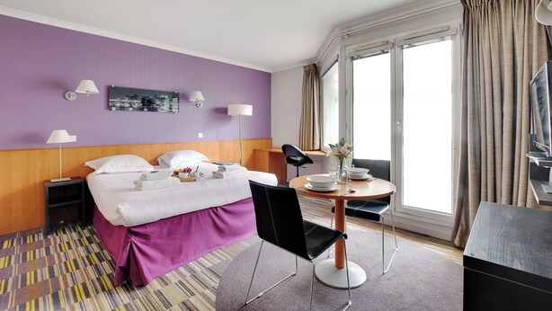 A hotel room with a bed, bedside tables, a desk with a chair, a window with curtains, and a television. - Modern Studio - 2P - Issy-les-moulineaux / Javel (La Courneuve)