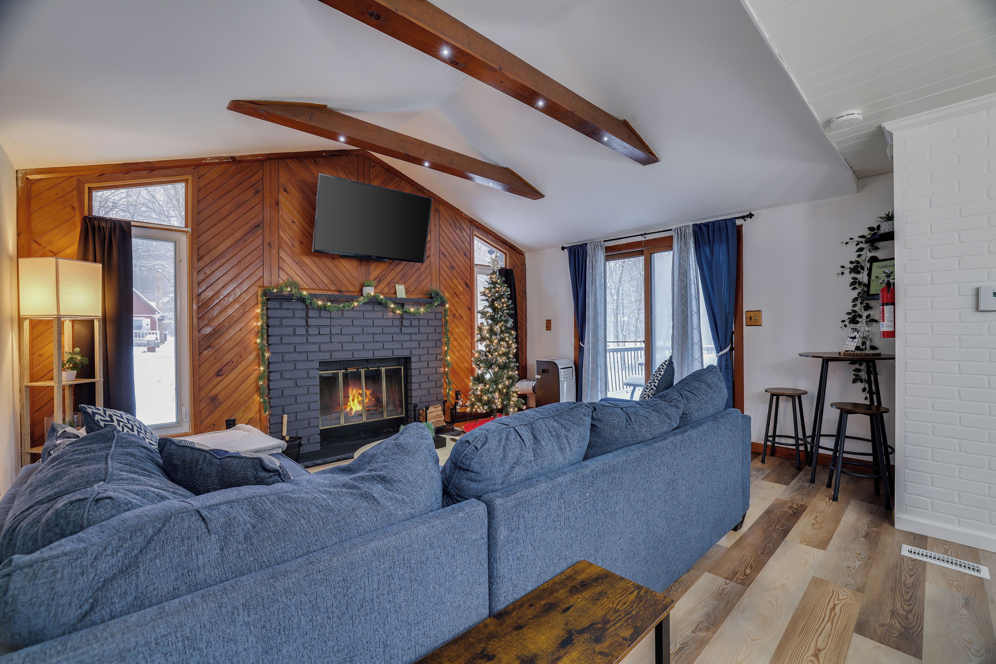 A modern living room with a large sectional sofa, a fireplace, a flat-screen TV, and a Christmas tree.