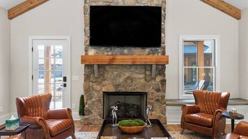 A living room with a stone fireplace, leather chairs, a coffee table, and a flat-screen TV mounted on the wall.