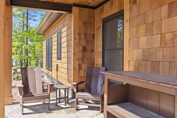 A wooden deck with outdoor furniture, including chairs and a table, and a large window.