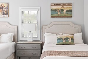 A bedroom with a bed, two nightstands, a window with blinds, and a wall with a Cruden Bay poster.