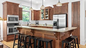 Uma cozinha com armários de madeira, eletrodomésticos de aço inoxidável, uma ilha grande com banquetas e iluminação pendente.