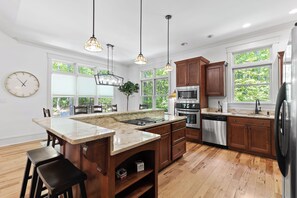 A modern kitchen with a large island, wooden cabinets, stainless steel appliances, and pendant lighting. - McLemore Resort - 84 Rushing Water Trail - Forest and Pond View (Rising Fawn)