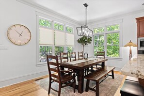 A dining area with a wooden table and chairs, large windows with blinds, a wall clock, and a hanging light fixture. - McLemore Resort - 84 Rushing Water Trail - Forest and Pond View (Rising Fawn)