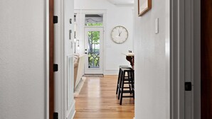 Um corredor com chão de madeira, uma porta que dá para uma sala com vista e um relógio de parede.