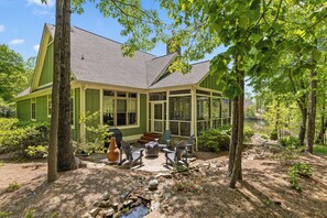 A green house with a porch, outdoor seating, and a view of a lake. - McLemore Resort - 84 Rushing Water Trail - Forest and Pond View (Rising Fawn)