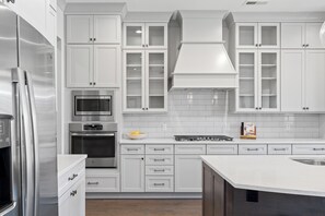 A modern kitchen with white cabinetry, stainless steel appliances, and a central island. - McLemore Resort - 156 Rushing Water Trail - Luxury Mountain Home (Rising Fawn)