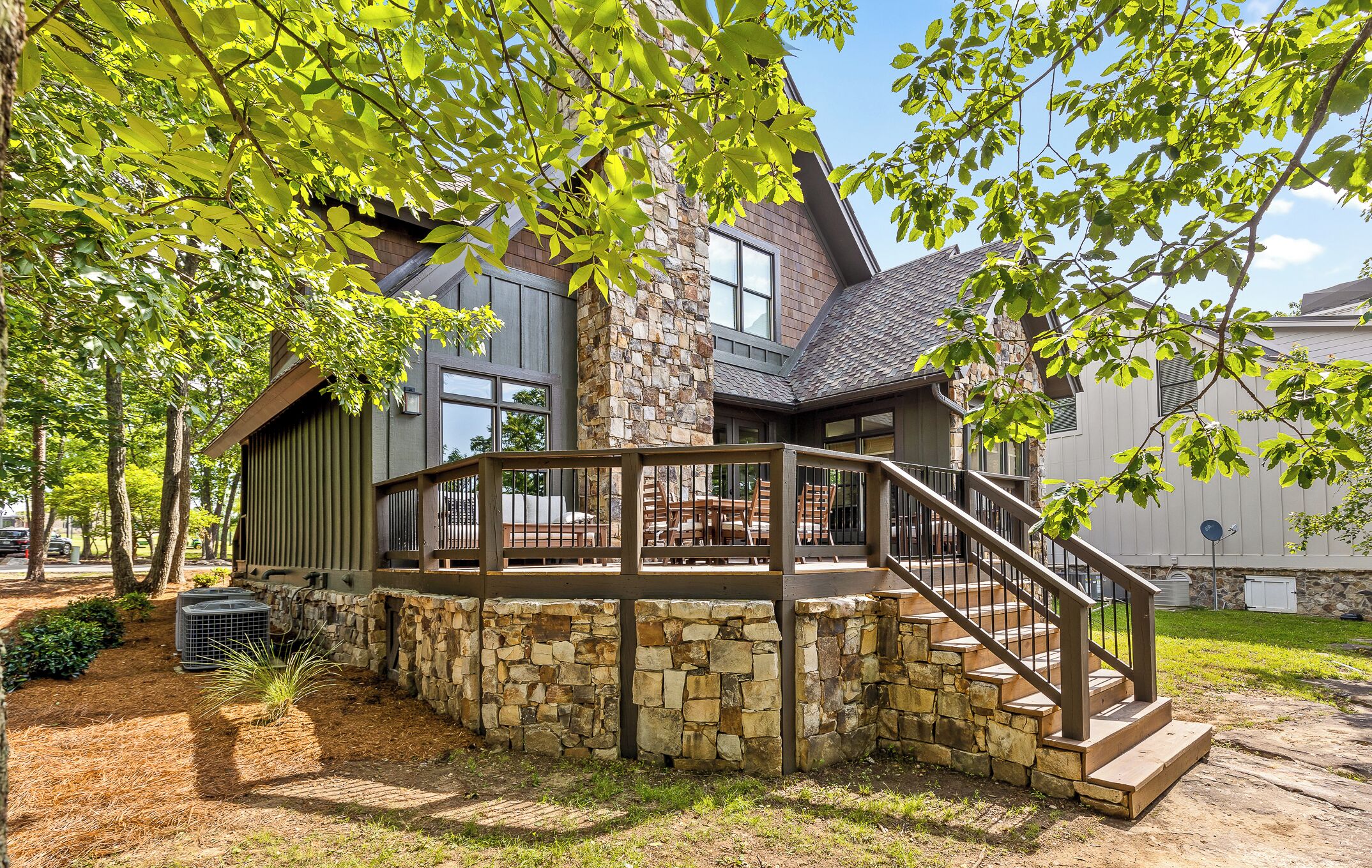 A modern house with a stone foundation, a wooden deck, and a staircase leading to a covered patio area.