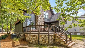A modern house with a stone foundation, a wooden deck, and a staircase leading to a covered patio area.