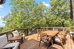 Une terrasse en bois, agréée de meubles d’extérieur, et entourée d’arbres.