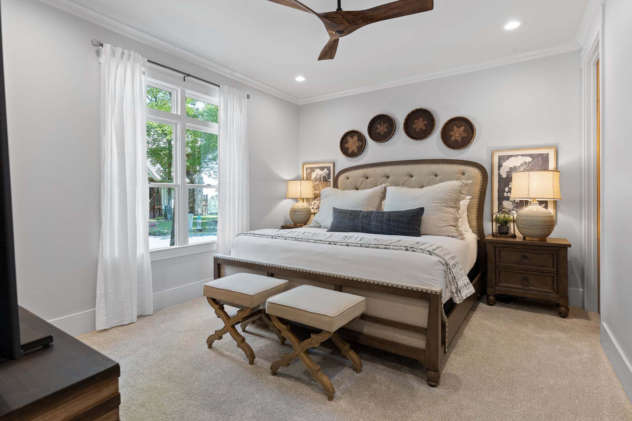 A bedroom with a bed, bedside tables, a ceiling fan, and a window with curtains.
