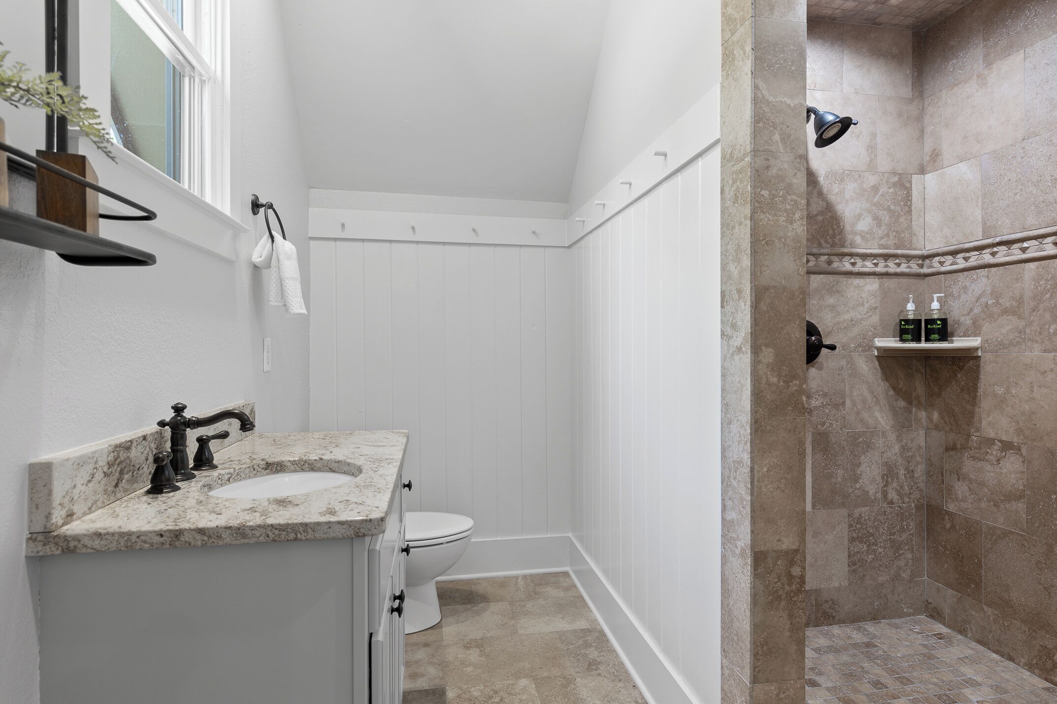 A bathroom with a white vanity, a toilet, and a shower area with beige tiles.