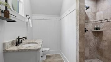 A bathroom with a white vanity, a toilet, and a shower area with beige tiles.