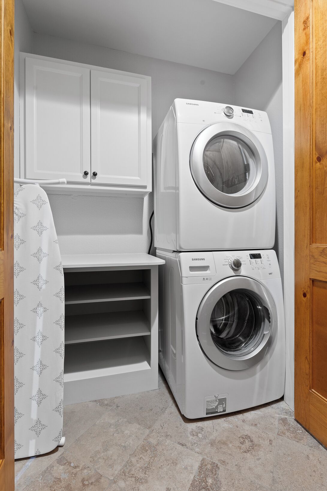 A laundry room with a stacked washer and dryer, a white cabinet, and a patterned shower curtain.