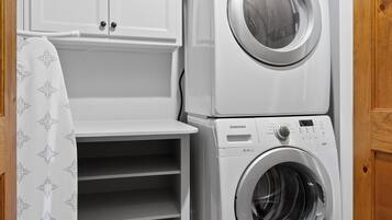 A laundry room with a stacked washer and dryer, a white cabinet, and a patterned shower curtain.