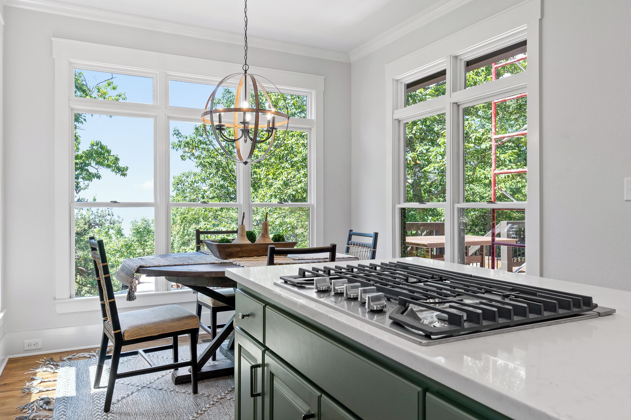 A kitchen with a central island, large windows, and a hanging light fixture.