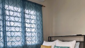 A bed with a beach-themed bedspread, a window with blue curtains, and a wall-mounted air conditioner. - Peaceful Studio Retreat Near Shoal Bay Beach - AC, Wi-Fi, Concierge Support (Shoal Bay Corner)