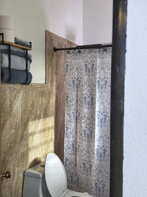 Ein Badezimmer mit Toilette, einem Handtuchhalter mit gefalteten Handtüchern und einer Duschvorhang mit Blumenmuster.