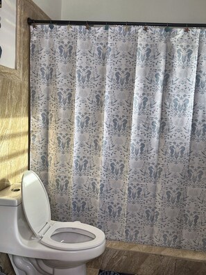 Ein Badezimmer mit Toilette, einer Duschvorhang mit Blumenmuster und einer Badewanne.