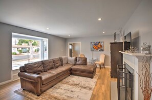 A spacious living room with a large brown leather sectional sofa, a small round table, and a chair. There is a fireplace with a mantel and a wall-mounted TV. - Walk 2 Sofi/Intuit/Forum Spacious 4bd/2ba Beautiful Inglewood Home (Inglewood)