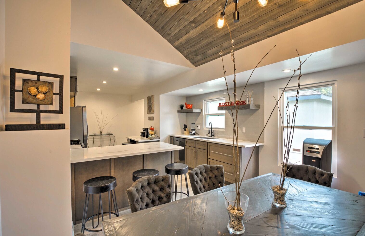 A modern kitchen with a central island, bar stools, and a dining table.