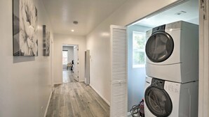 A laundry room with two stacked washing machines, a wooden floor, and a hallway leading to another room. - Walk 2 Sofi/Intuit/Forum Spacious 4bd/2ba Beautiful Inglewood Home (Inglewood)