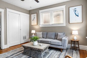 A living room with a grey sofa, a coffee table, a potted plant, and two wall-mounted lamps. - The Cove | A St. Louis Retreat by StayLage (Saint Louis)